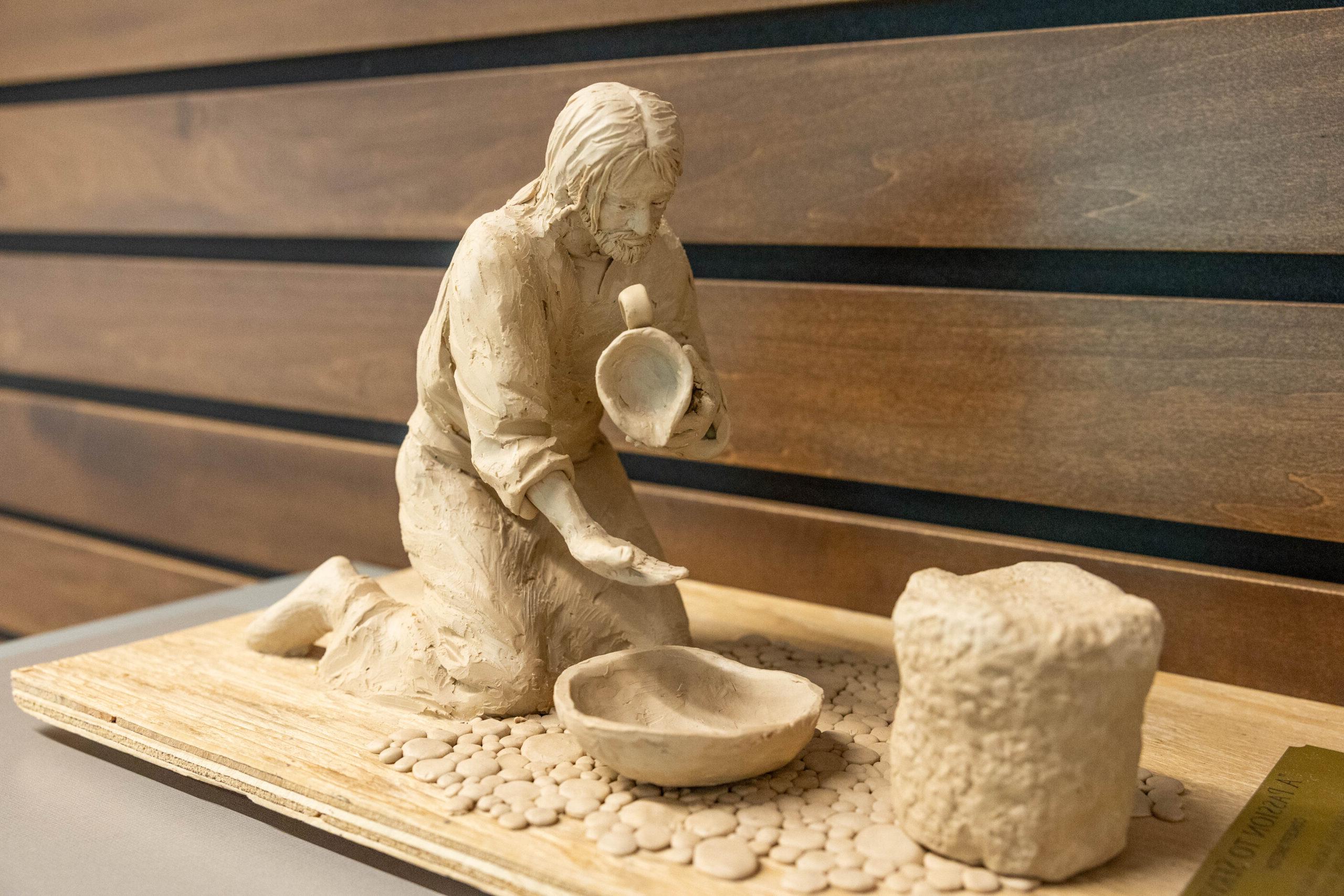 Passion to Serve sculpture rendering in clay. Figure kneeling, pouring water into a bowl